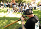 Man playing didgeridoo with people sitting on grass in front of him.